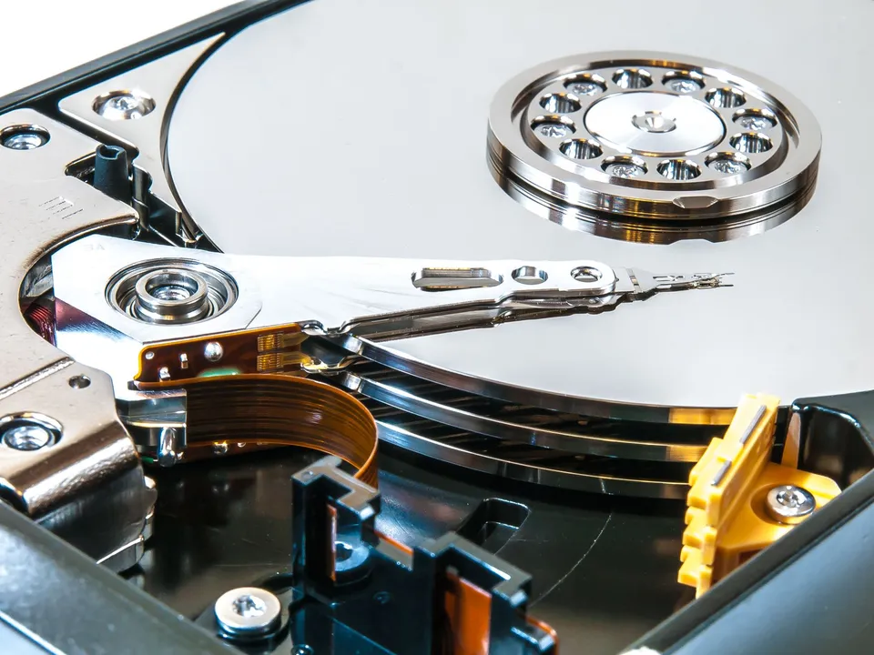 The inside of a hard drive, its platter and read arm exposed, representing server and database migration