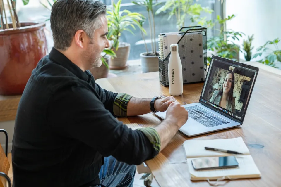 A senior engineer on a one-to-one video consulting call, taking notes beside a laptop