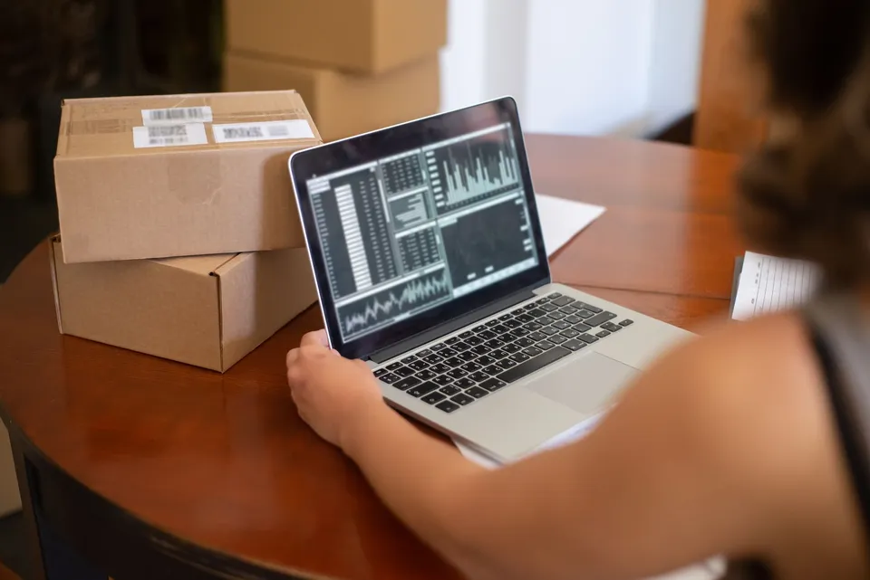 A person reviewing a dashboard on a laptop beside stacked shipping boxes