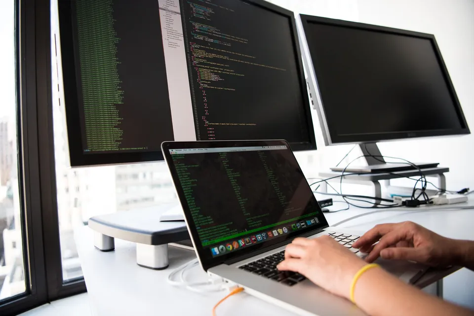 A developer working across three monitors with code editors open, running work across multiple platforms