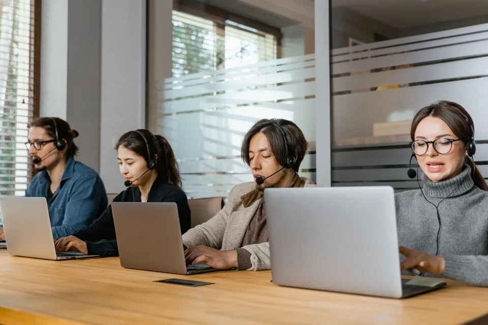 A support team at laptops with headsets, answering technical questions directly